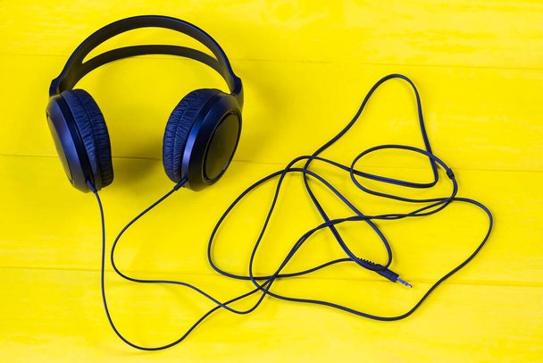 wooden background in yellow retro style. On it are black headphones and part of the wire. - Photo, Image