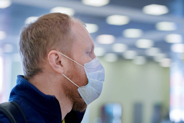 Ο Ευρωπαίος κοκκινογένης φοράει προστατευτική ιατρική μάσκα στο αεροδρόμιο.  - Φωτογραφία, εικόνα