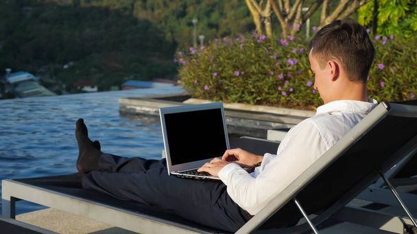 İş adamı dizüstü bilgisayarla orman ve otel havuzuna karşı çalışıyor - Fotoğraf, Görsel