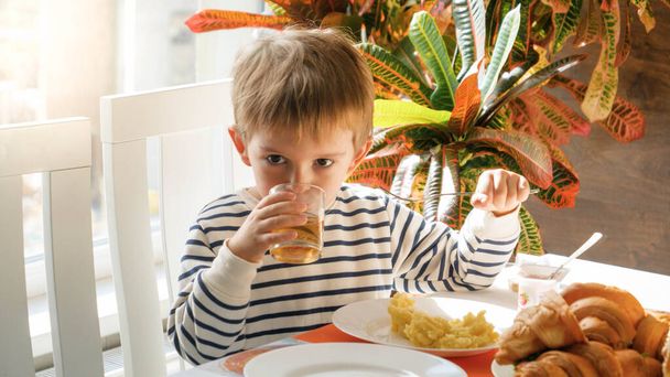 Porträt des süßen kleinen Jungen trinkt Gjuice, während er im Speisesaal reakfastet - Foto, Bild