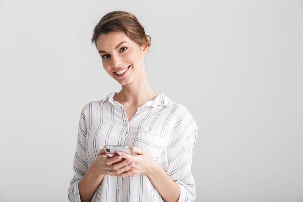 Image of joyful beautiful woman smiling and using mobile phone isolated over white background - Fotó, kép