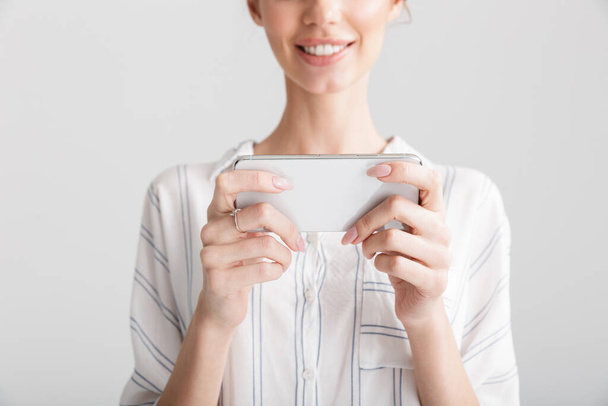 Cropped image of beautiful woman smiling and playing video game on cellphone isolated over white background - Fotografie, Obrázek