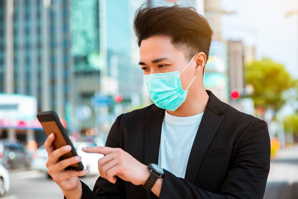 młody biznesmen noszący maskę na ulicy i obserwujący telefon komórkowy - Zdjęcie, obraz