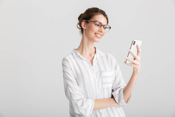 Image of joyful beautiful woman in eyeglasses typing on mobile phone isolated over white background - Foto, afbeelding