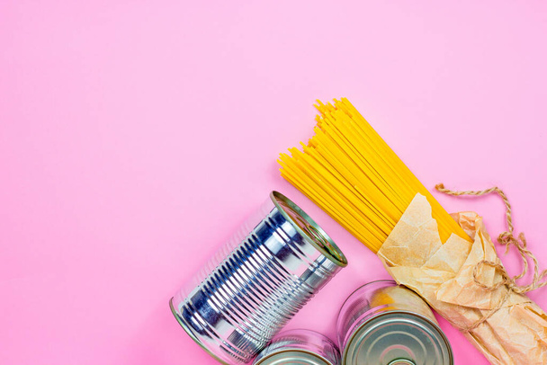 Comida enlatada, latas de metal e macarrão de espaguete amarelo no fundo rosa com espaço de cópia. Conceito de doação, entrega e caridade. - Foto, Imagem