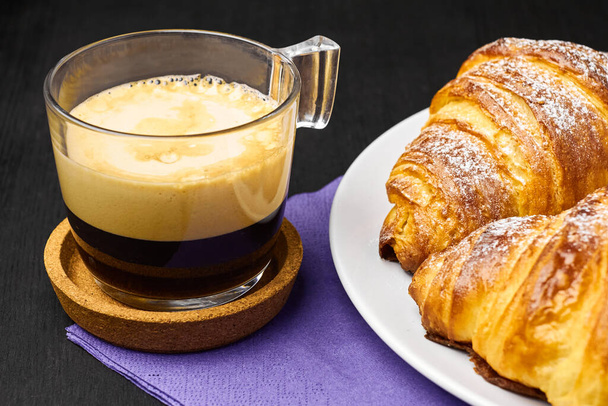 Feche uma xícara de café expresso e croissants frescos em um serviette roxo. Conceito de café da manhã em um fundo preto
 - Foto, Imagem