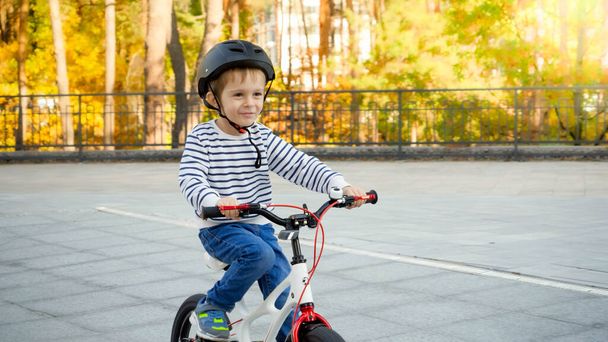 Portrait of cute 3 years old little boy in protective helmet riding bicycle at public park - Foto, immagini