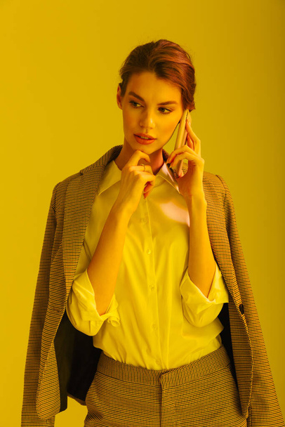 Image of serious pretty woman in formal suit talking on cellphone isolated over yellow background - Foto, Imagem