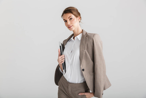 Image of serious pretty woman in formal suit posing with laptop on camera isolated over white background - Foto, imagen
