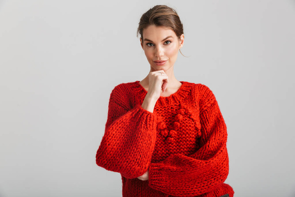 Image of pleased pretty woman in red sweater posing and looking at camera isolated over white background - Zdjęcie, obraz