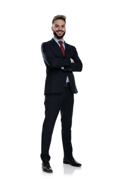 glücklicher junger Geschäftsmann verschränkt die Arme und lächelt, isoliert auf weißem Hintergrund stehend - Foto, Bild
