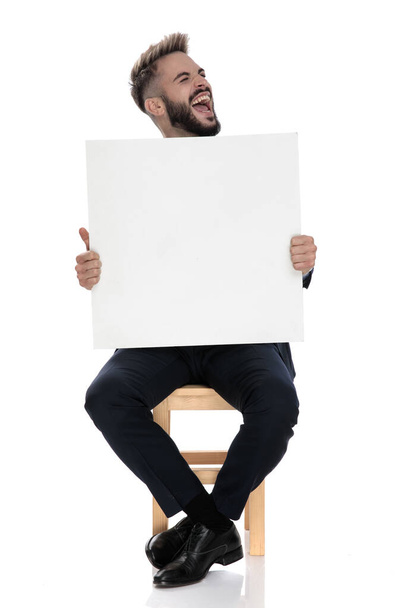 young businessman holding empty board and screaming, sitting isolated on white background - Photo, Image