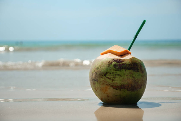 fresh coconut with chopped top and straw stands on wet sand - Foto, Bild