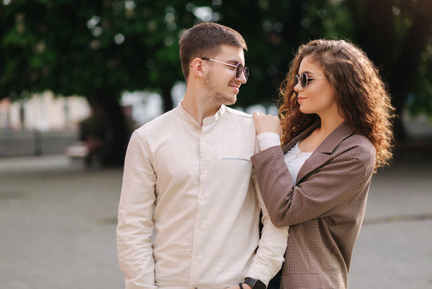 Happy couple walking in the city. Attractive young woman with curly hair and handsome young man in centre of the city. Smiled people in sunglasses outdoors - Foto, afbeelding
