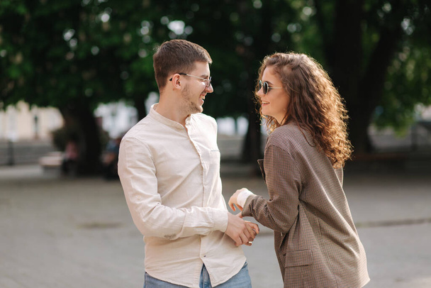 Happy couple walking in the city. Attractive young woman with curly hair and handsome young man in centre of the city. Smiled people in sunglasses outdoors - Photo, Image