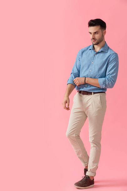 handsome businessman wearing blue shirt standing and looking away while fixing sleeve with style on pink studio background - 写真・画像