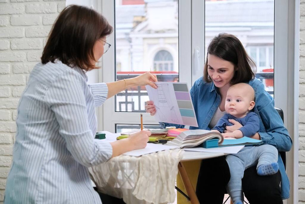 Mulheres designer de interiores e cliente com bebê escolhendo tecidos e materiais
 - Foto, Imagem
