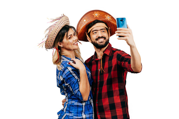 Brazilian couple wearing traditional clothes for Festa Junina - June festival. Couple taking self portrait on cell phone - Фото, изображение