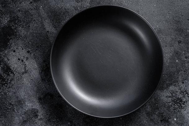 Black plate on textured black background. Top view. Copy space. - Foto, imagen