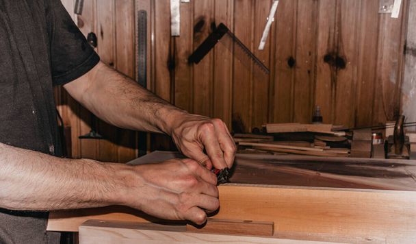 closeup scene of a male carpenter working in carpentry workshop, planing a wood piece with a double hand push woodworking bird planer. - Photo, Image