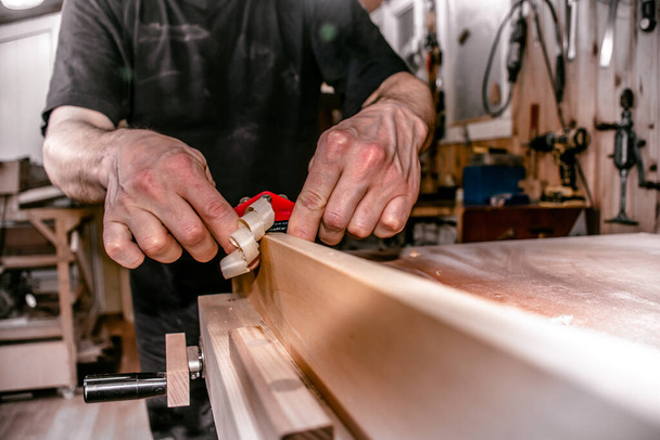 een mannelijke timmerman werkt in atelier, schaven een houten stuk met een dubbele hand duwen houtbewerking vogelschaafmachine, close-up.  - Foto, afbeelding