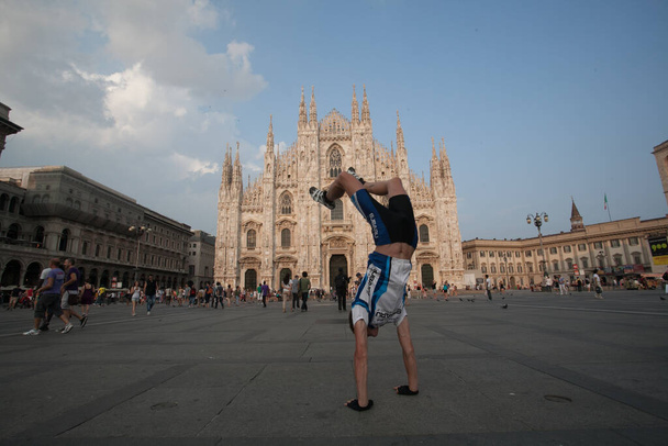 Male tourist cyclist funny posing on handstand on the background of the Duomo di Milano on a sunny summer day in the crowd square. Milan Italy, Milan July 13, 2013. - Photo, image