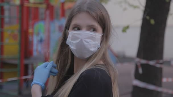 Girl in medical mask and rubber gloves on street. Woman removes and puts on medical mask in bad weather. Close-up young woman Slavic appearance. Concept of protection from viruses. Covid-19 pandemic - Materiał filmowy, wideo