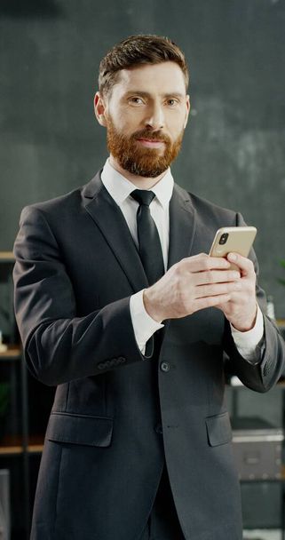Portrait of Caucasian joyful businessman in office texting message on smartphone. - Valokuva, kuva