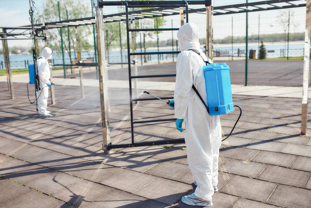 Working safely. Sanitization, cleaning and disinfection of the city due to the emergence of the Covid19 virus. Specialized team in protective suits and masks at work near sports ground - Zdjęcie, obraz