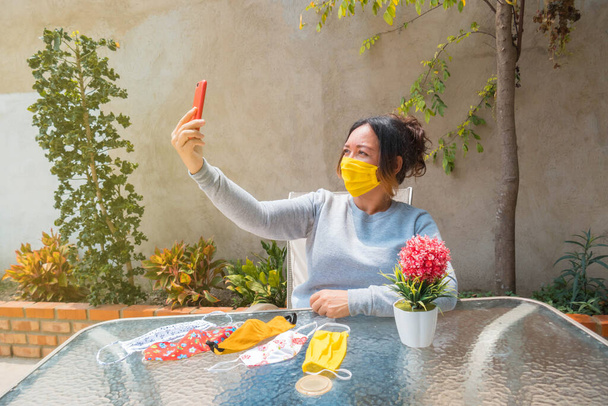 woman with a face mask sitting at home taking pictures with her cell phone - Photo, Image