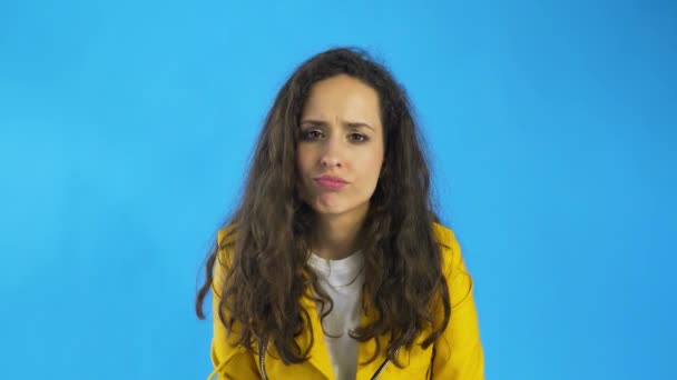 Sad thoughtful young beautiful woman shrugging in Studio with blue Background. - Footage, Video