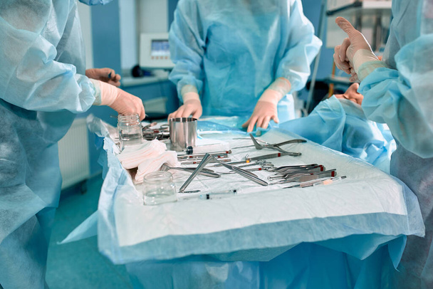 Стерильні інструменти на операційному столі, команда лікарів викладає інструменти для операції. багато рук заварюють у стерильних рукавичках
. - Фото, зображення