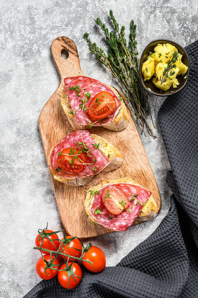 Canapes with salami salchichon, cherry tomatoes and micro greens on a baguette. gray background. top view. - Photo, Image