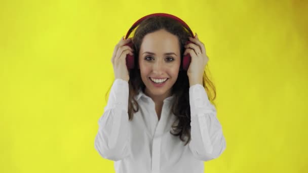 Woman listening to music with red headphones in Studio with yellow Background. - Imágenes, Vídeo