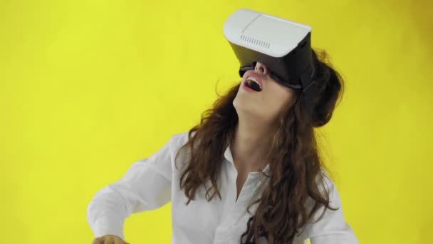 Happy young woman with virtual reality headset or 3d glasses on yellow background at studio. - Imágenes, Vídeo