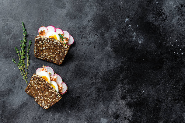 Toast from grain bread with hot smoked salmon, egg and radish. Black background, top view, space for text. - Fotó, kép