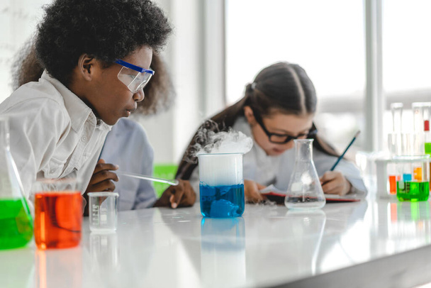 Groupe d'adolescents mignons petits élèves apprenant la recherche et faisant une expérience chimique tout en faisant analyser et mélanger du liquide dans une éprouvette dans une classe de laboratoire expérimental à l'école.Éducation - Photo, image