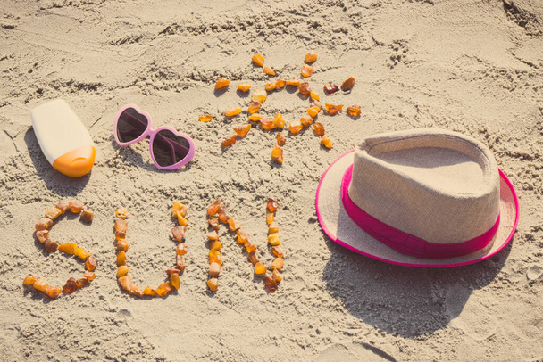ビーチで砂の上に琥珀色の石、サングラス、太陽化粧水とわら帽子で作られた太陽のヴィンテージ写真、碑文と形状、日光浴の概念、夏と休暇の時間 - 写真・画像