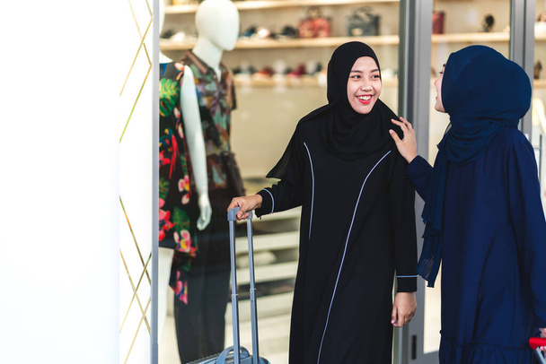 Dwie młode muzułmanki azjatyckie cieszące się zakupami i zabawą wskazując palcem w witrynie sklepu na świeżym powietrzu w sklepie odzieżowym - Zdjęcie, obraz