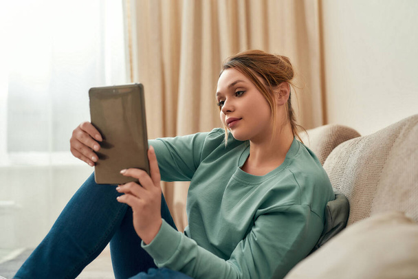 Surfing internet. Young beautiful girl in casual clothes relaxing on sofa in the living room at home and using digital tablet - Φωτογραφία, εικόνα