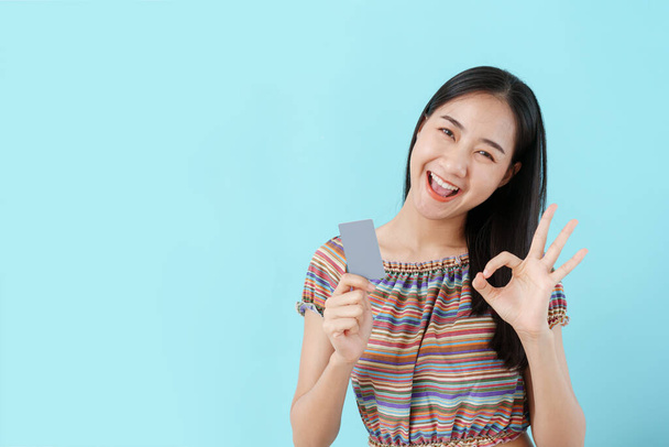 Mooi jong Aziatisch meisje met blanco creditcard en ok hand vrouwen op de achtergrond blauw geïsoleerd. Azië vrouwen blij glimlach en kopieer ruimte  - Foto, afbeelding