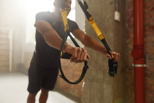 Remove weakness. Athletic young man doing fitness TRX training exercises at industrial gym - Foto, Imagem