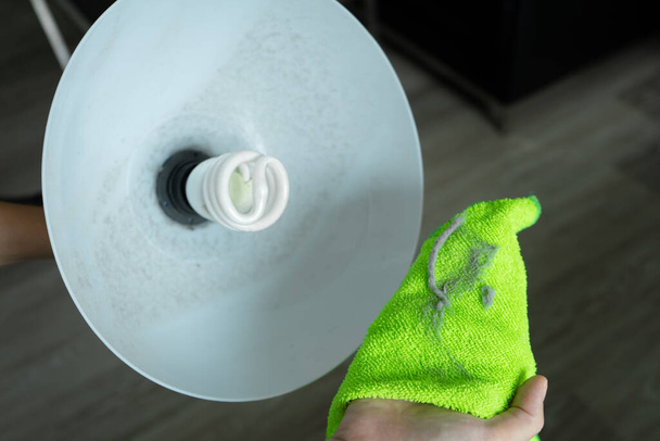 Limpiando la casa. Limpie el polvo con un trapo verde de la lámpara de pie. Bombilla de ahorro de energía. Mucho polvo.
 - Foto, Imagen