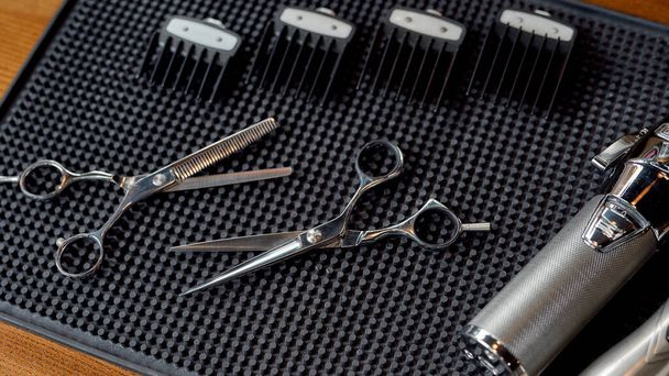 Ready for work. Top view of scissors, electric hair clipper and four different nozzles lying on a rubber mat in the barbershop. Professional barber tool kit - Foto, immagini