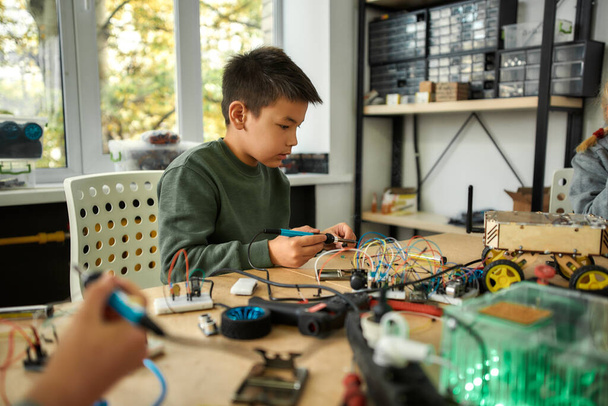 Passion that builds excellence. Young engineer using soldering iron to join chips and wires. Robotics and software engineering for elementary students. Inventions and creativity for kids - Foto, Bild