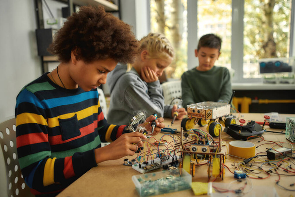 応用知能の力。チップやワイヤーに参加するためにハンダ鉄を使用して若いエンジニア。小学生のためのロボット工学とソフトウェア工学.子供のための発明と創造性 - 写真・画像