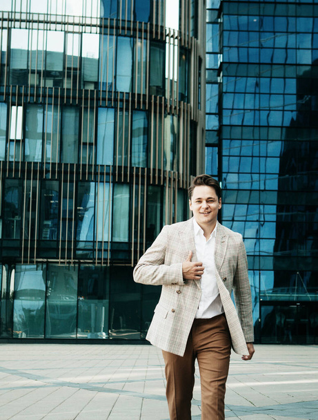 Young happy man in a business suit poses near a modern business center on a summer day - Photo, Image