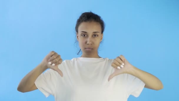 Menina bonita em uma camiseta branca mostra polegar para baixo com ambas as mãos no fundo azul
 - Filmagem, Vídeo