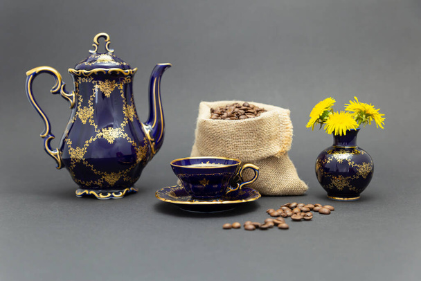 zátiší s krásným kobaltově modré barevné vinobraní porcelánu káva set se zlatým květinovým vzorem, květinová váza a gunnysack plněné pražených kávových zrn. - Fotografie, Obrázek