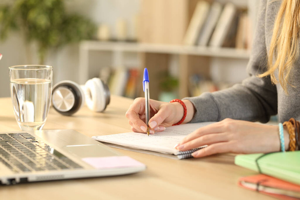 Закрыть руки студентки, пишущей на блокноте, делая домашнее задание на столе
 - Фото, изображение